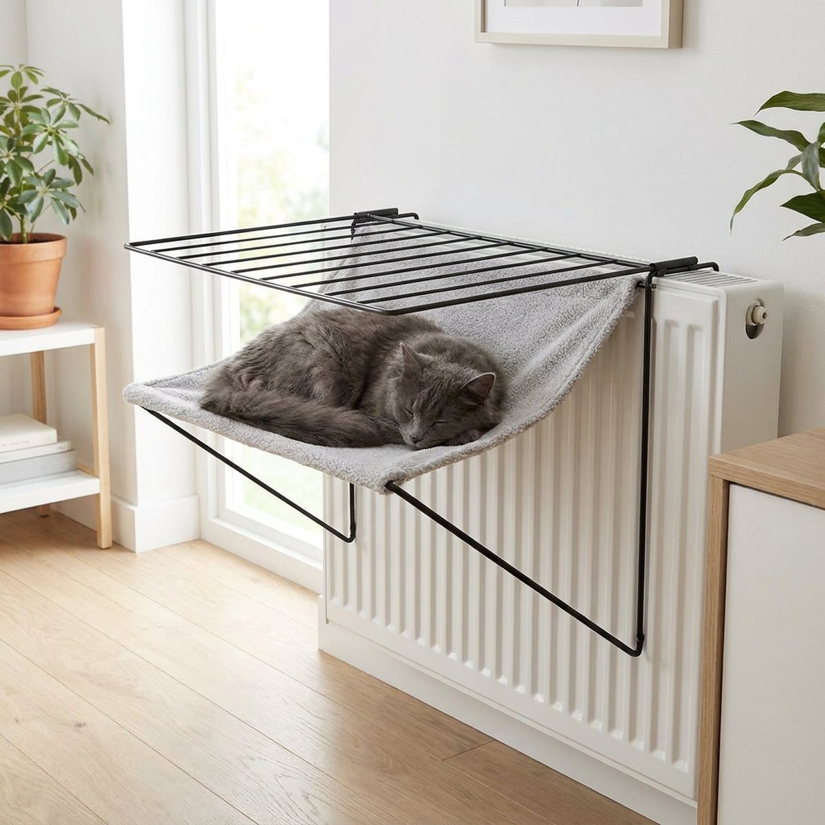 Grå katt som ligger avslappnad på en grå kattbädd monterad på ett vitt element vid ett fönster