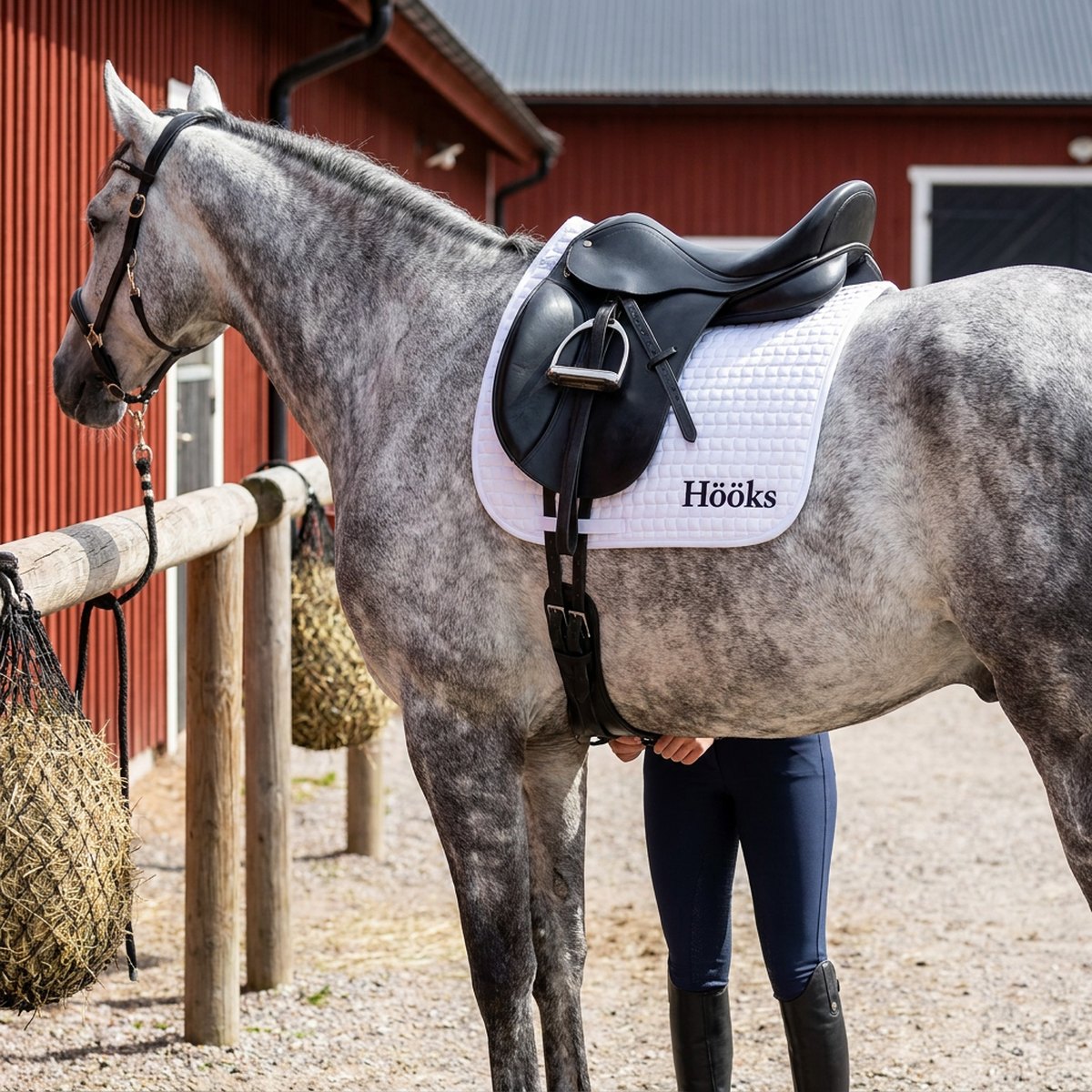 Vitt Hööks-schabrak med broderad logga och vågquiltning på grå häst vid skandinavisk stall